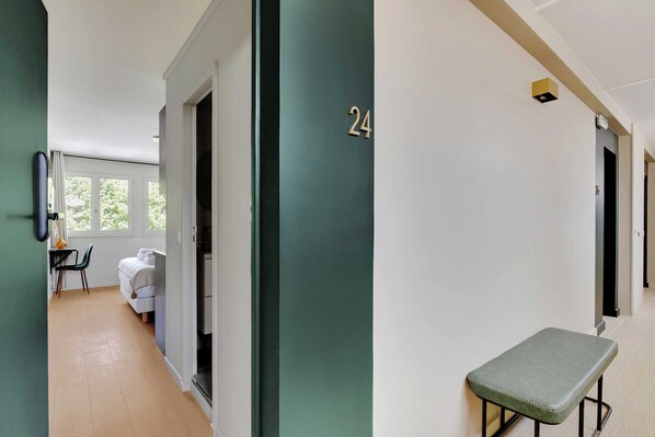 A hallway with a green door marked with the number 24, a bench, and a bed in the background. - Modern "green Suites" Residence - Meudon/velizy (Meudon)