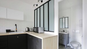 A modern kitchen with a sink, toaster, and kettle, and a bathroom with a toilet and mirror. - Welcoming Studio for 2 People - Bastille (Paris)