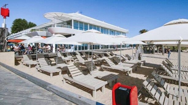 A beachside area with sun loungers and umbrellas, a building with large windows, and a clear blue sky. - This apartment is a 2 bedroom(s), 2 bathrooms, located in Fremantle, WA. (Fremantle)