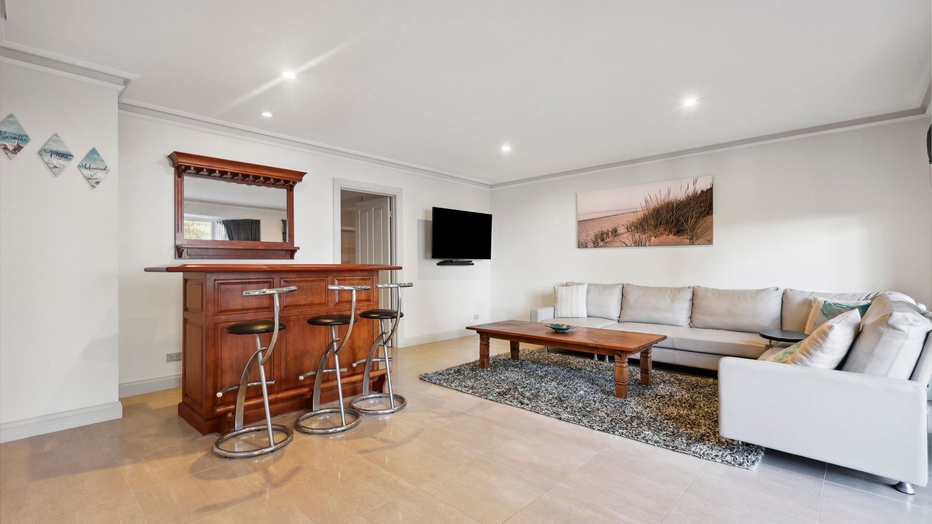 A modern living room with a wooden bar, a sofa, a coffee table, and a TV mounted on the wall.