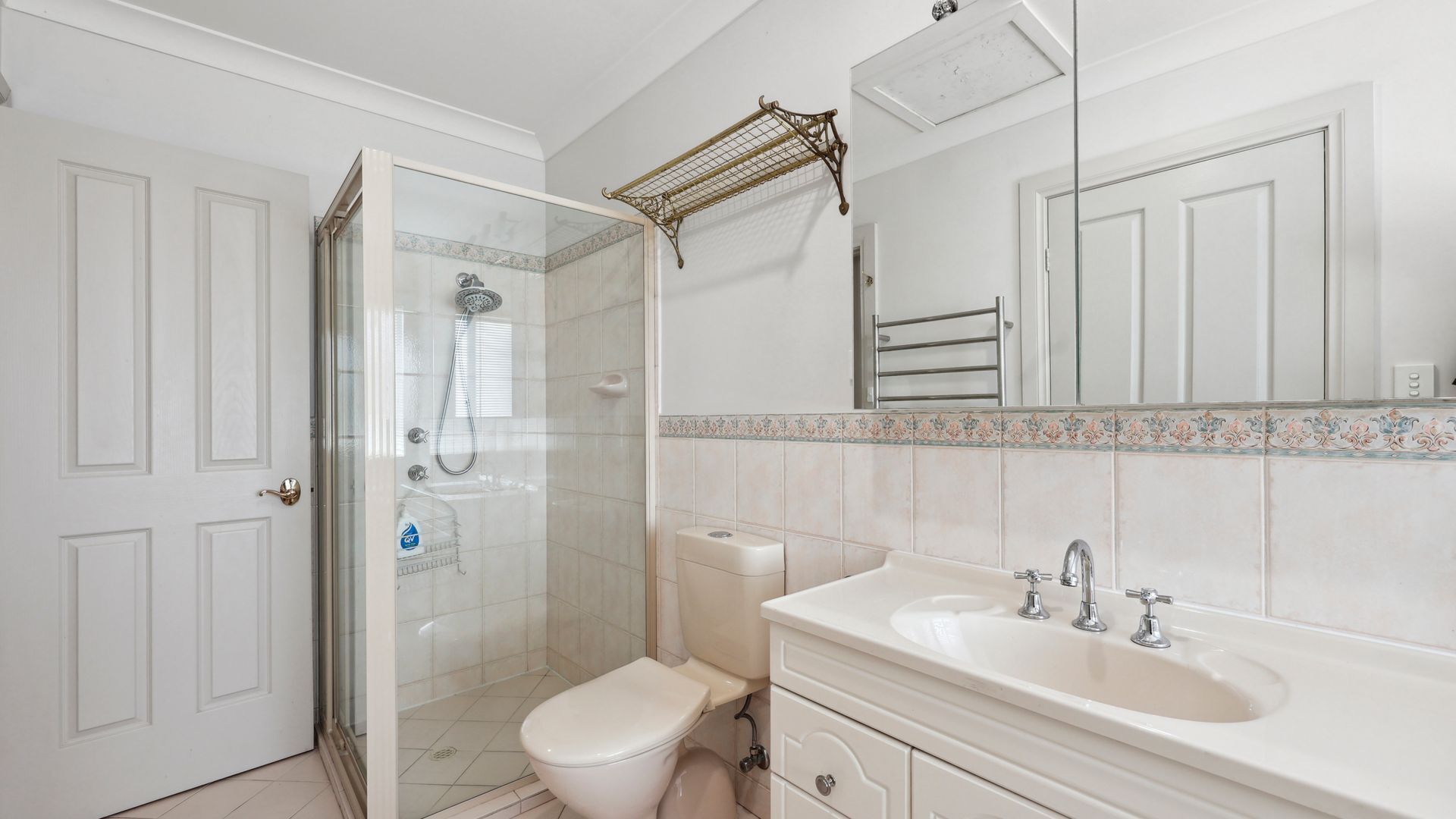 Un bagno con doccia vetrata, un water, un lavandino e uno specchio con cornice in piastrelle decorative.