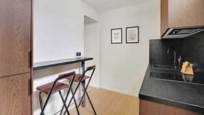 Una cucina compatta con un piano di lavoro nero, una sedia pieghevole e due quadri appesi al muro.