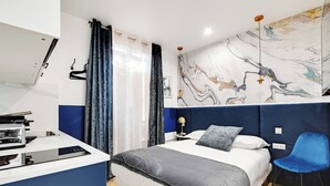 A modern hotel room with a bed, a desk with a computer, a chair, and a large abstract painting on the wall. - Charming Studio - 2P With AC Near Montmartre (Paris)