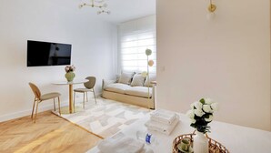 A modern living room with a sofa, a dining table, and a TV mounted on the wall. - Peaceful Chic Studio - 2P - Arc de Triomphe (Paris)