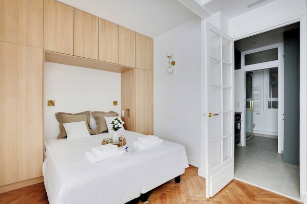 A modern bedroom with a wooden headboard, a neatly made bed with white linens, and a small bedside table with a vase and a book. - Peaceful Chic Studio - 2P - Arc de Triomphe (Paris)