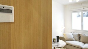 A room with a wooden wall, a digital thermostat, a round table with a candle, and a beige sofa. - Peaceful Chic Studio - 2P - Arc de Triomphe (Paris)