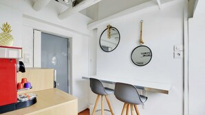 Una cucina compatta con macchina da caffè, due sgabelli e un piano di lavoro bianco.
