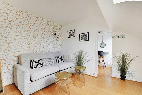 Un salon moderne avec un canapé gris, un papier peint à motifs et deux plantes en pot.