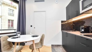 Una cocina moderna con armarios oscuros, una encimera blanca y un microondas. Hay una mesa de comedor con dos sillas y una copa de vino.