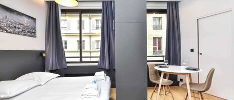 Une chambre d’hôtel moderne avec un lit, une table à manger et des chaises, et une vue sur la ville par la fenêtre.