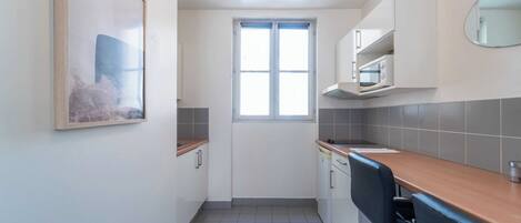 A compact kitchen with a window, white cabinets, a microwave, and a wooden countertop.