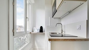 A compact kitchen with a built-in oven, a sink, and a window overlooking a cityscape. - Cosy Studio for 2 People - Malakoff (Malakoff)
