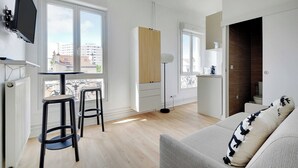 A modern apartment with a balcony, a dining area with stools, a sofa, and a TV mounted on the wall. - Cosy Studio for 2 People - Malakoff (Malakoff)