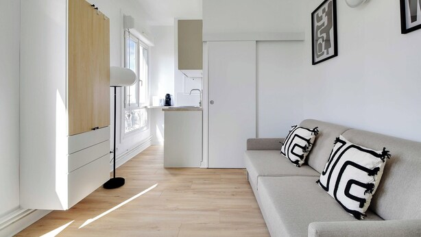 A modern, minimalist living room with a sofa, a floor lamp, and a small kitchen area. - Cosy Studio for 2 People - Malakoff (Malakoff)