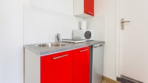 Eine kompakte Küche mit Spüle aus Edelstahl, einer Mikrowelle und roten Schränken.