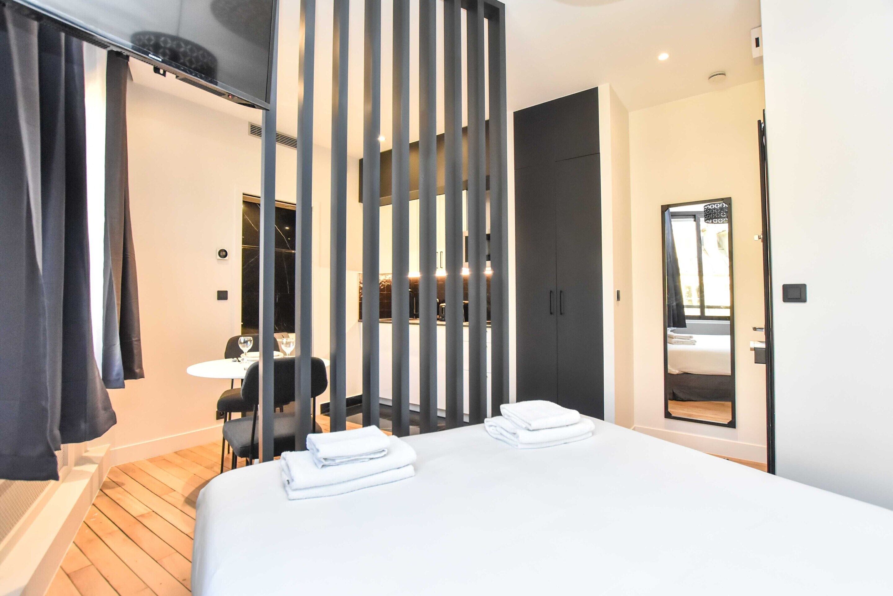 Ein modernes Hotelzimmer mit einem großen Bett, einem Schreibtisch mit Stuhl, einem kleinen Tisch mit Glas und einem Spiegel an der Wand.