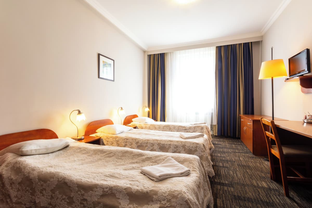 Habitación de hotel con dos camas, un escritorio, una silla, un televisor y una ventana con cortinas.