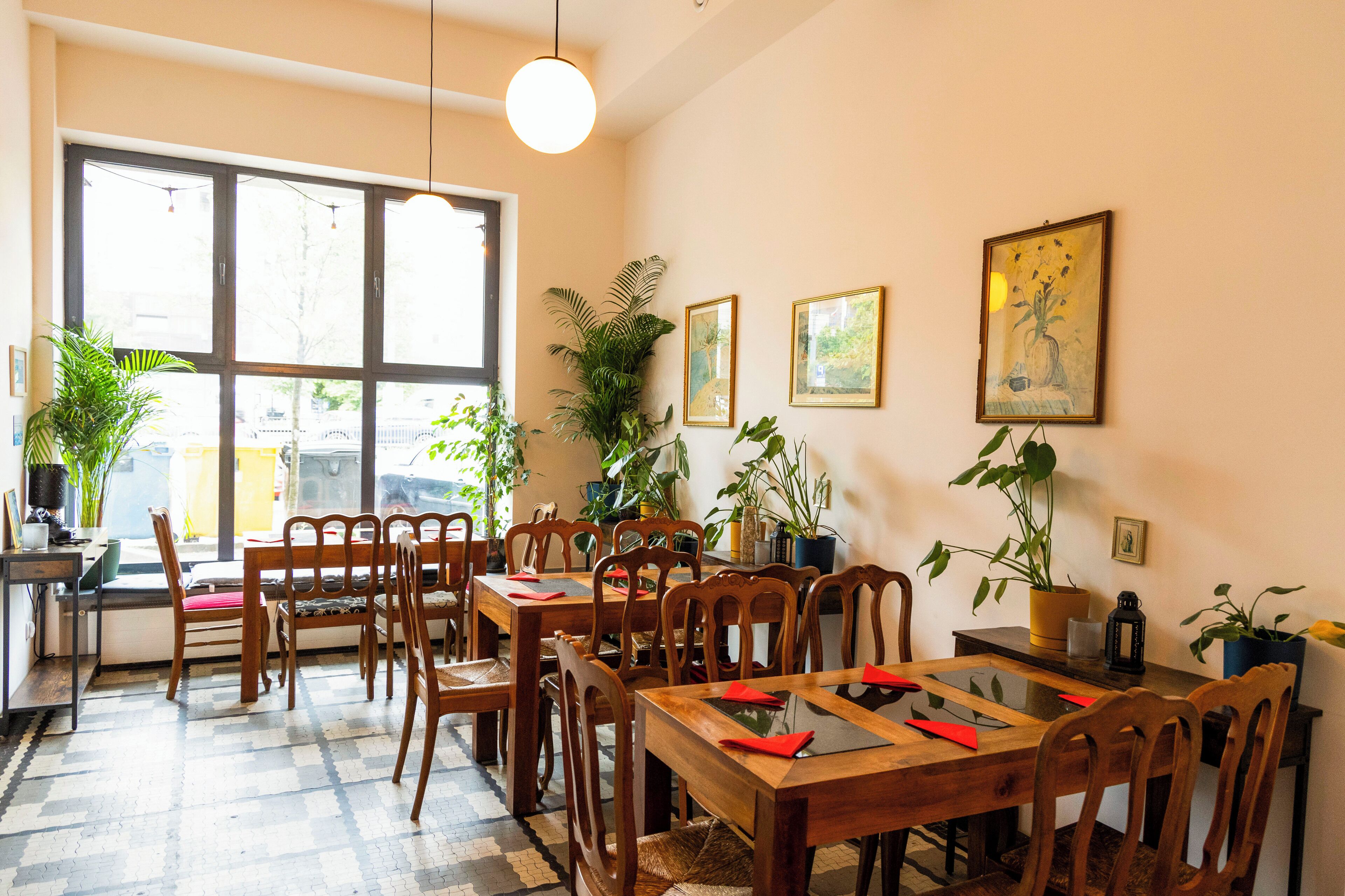 Zona pranzo con tavoli e sedie in legno, piante in vaso e quadri appesi alle pareti.