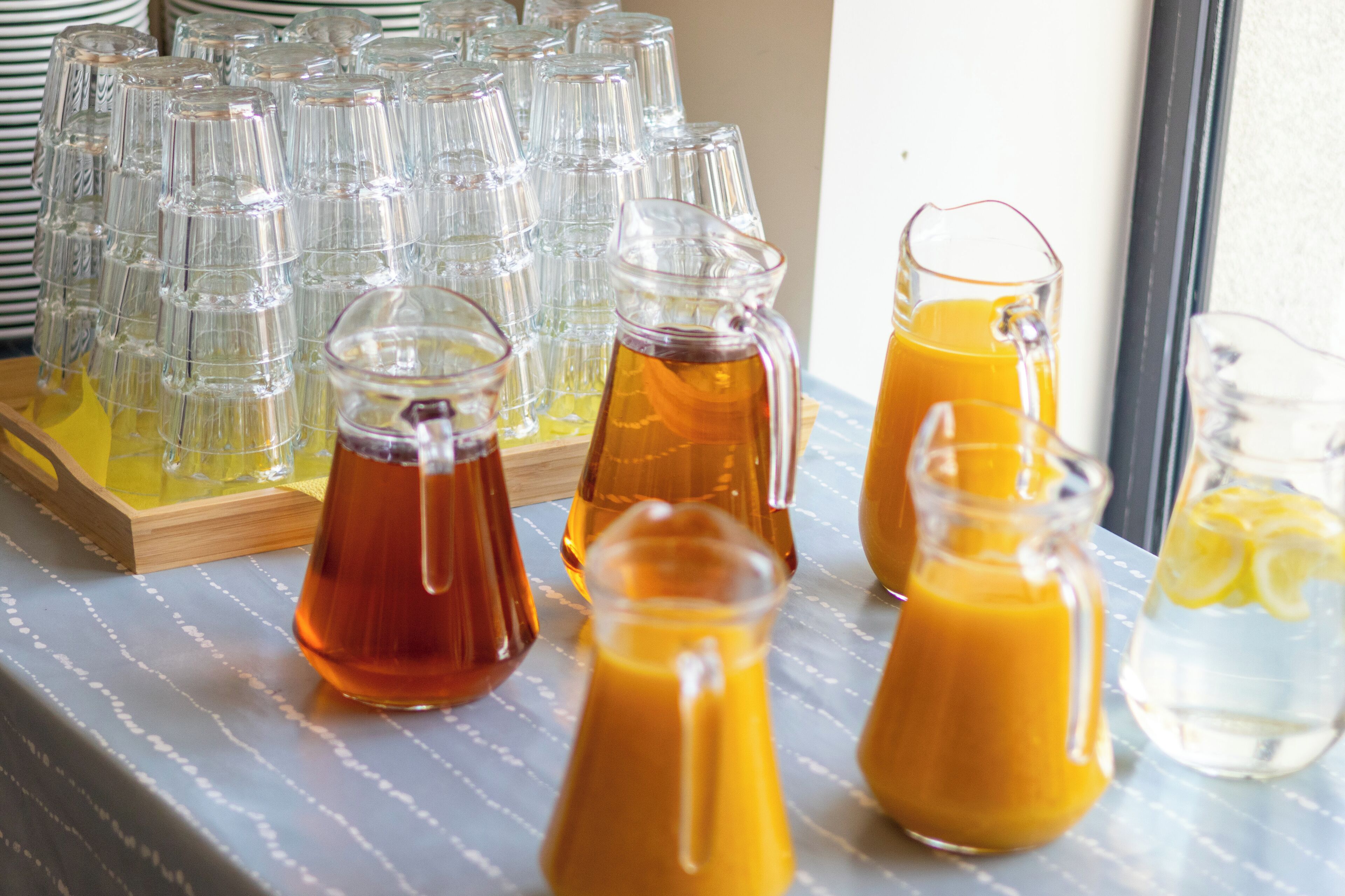 Una mesa con varios recipientes de vidrio con bebidas, como jugo de naranja y té helado, sobre un mantel a rayas.