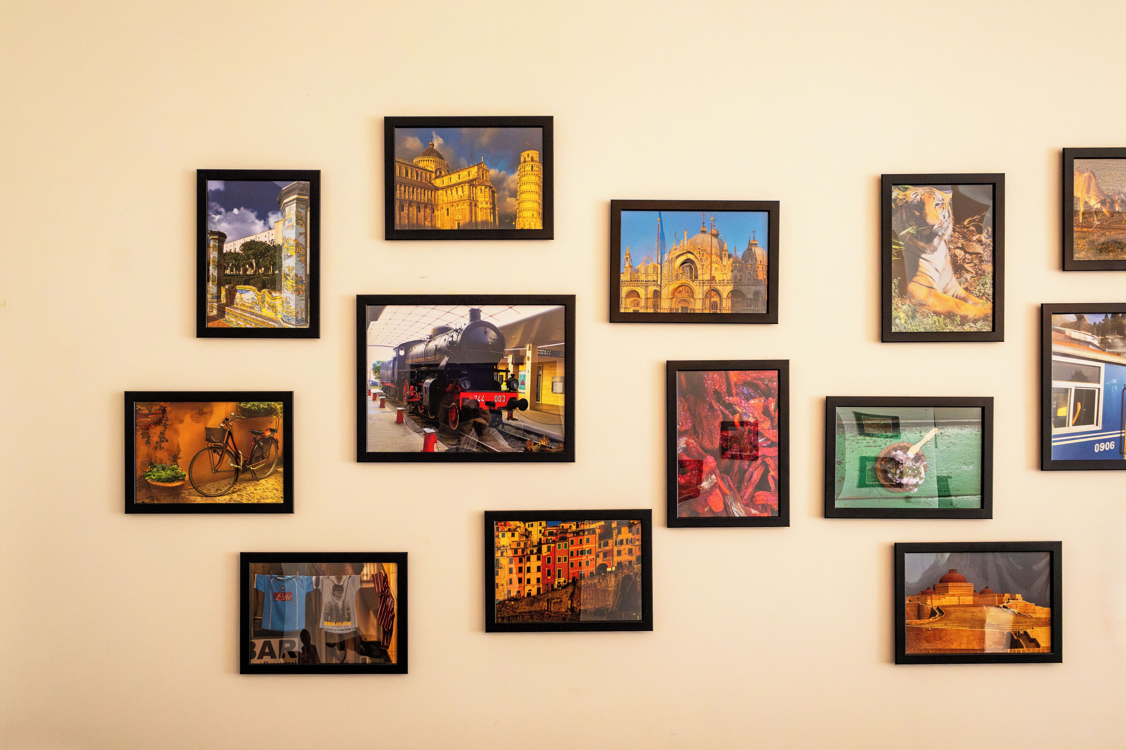 Una parete con diverse foto incorniciate di edifici, una bicicletta e un treno.