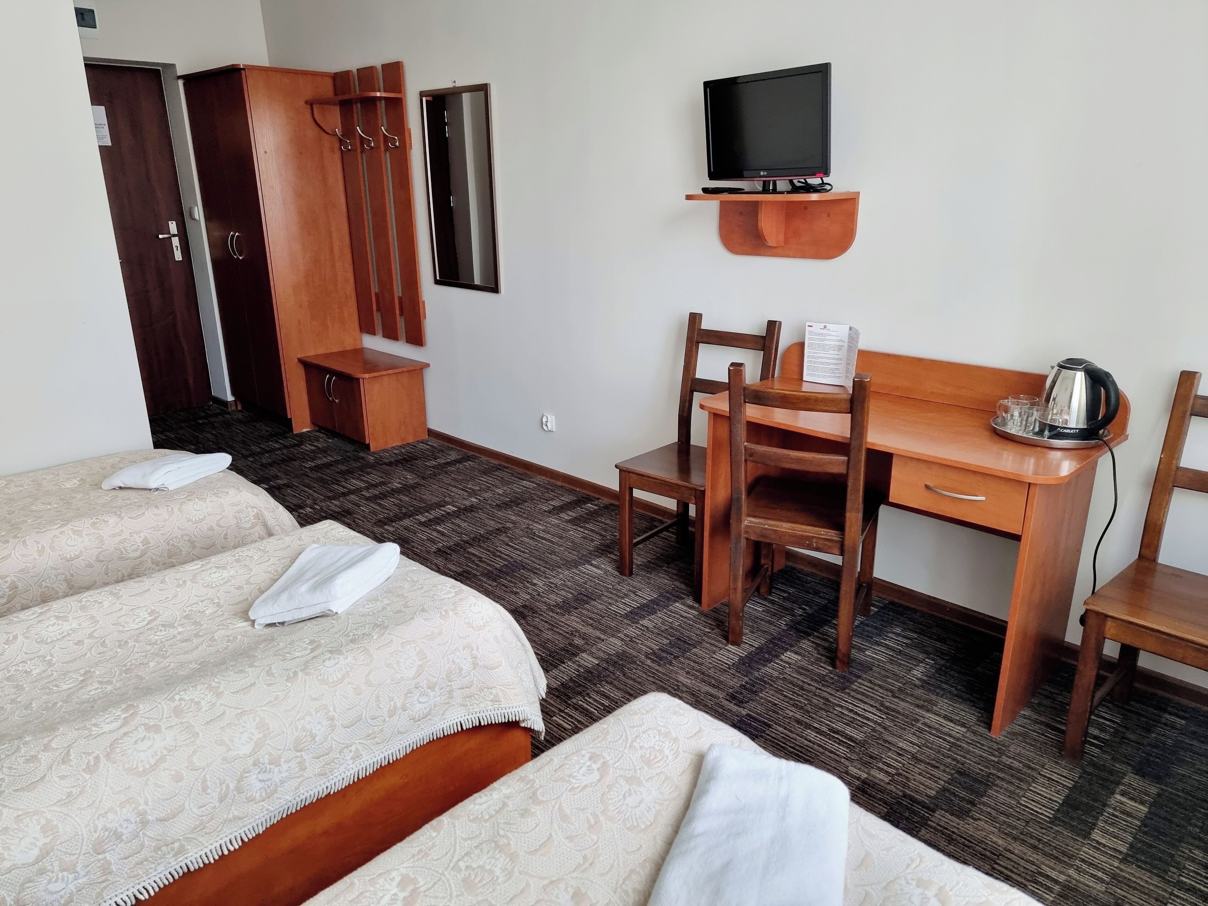 Habitación de hotel con dos camas, un escritorio con silla, un televisor y una tetera.