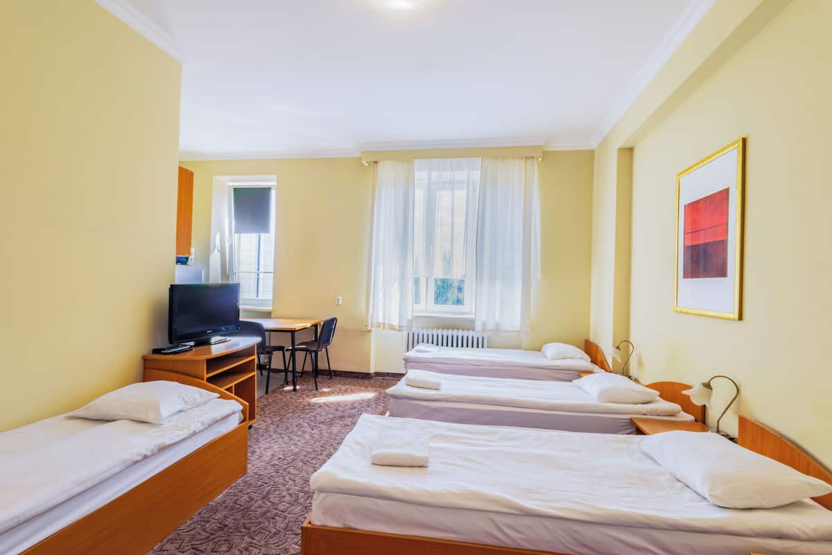 Habitación de hotel con cuatro camas individuales, un escritorio con silla, televisor y ventana con cortinas.