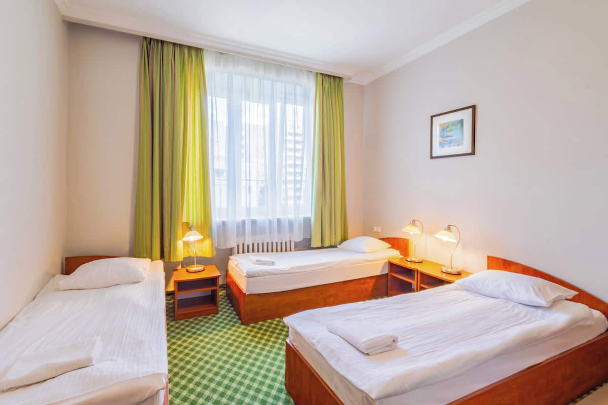 Habitación de hotel con dos camas individuales, piso a cuadros, una ventana con cortinas verdes y dos lámparas de noche.