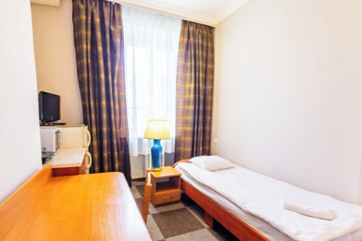 A small hotel room with a single bed, a wooden desk, a lamp, and a television on a stand.