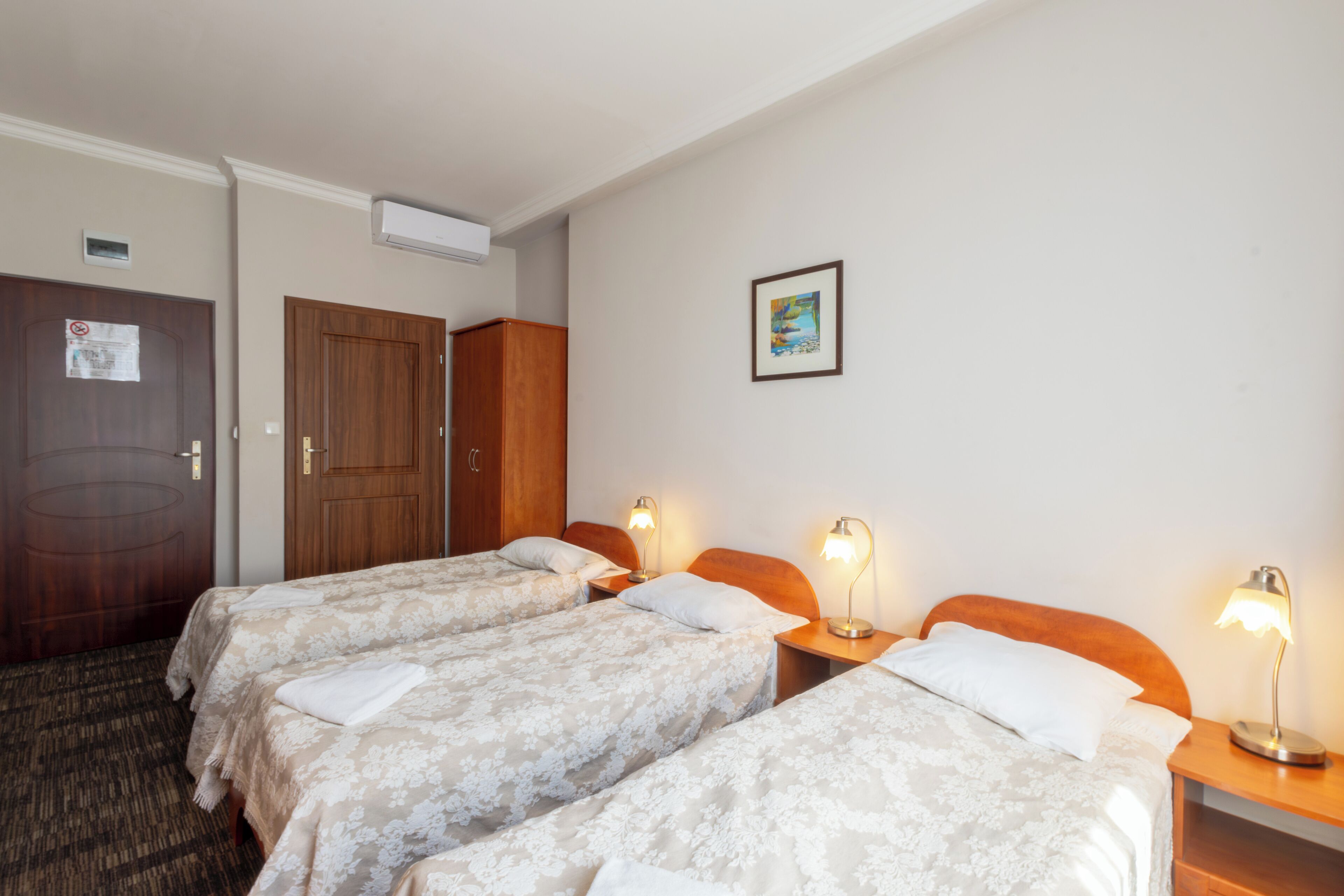 Una habitación de hotel con tres camas, cabeceros de madera y lámparas de noche.