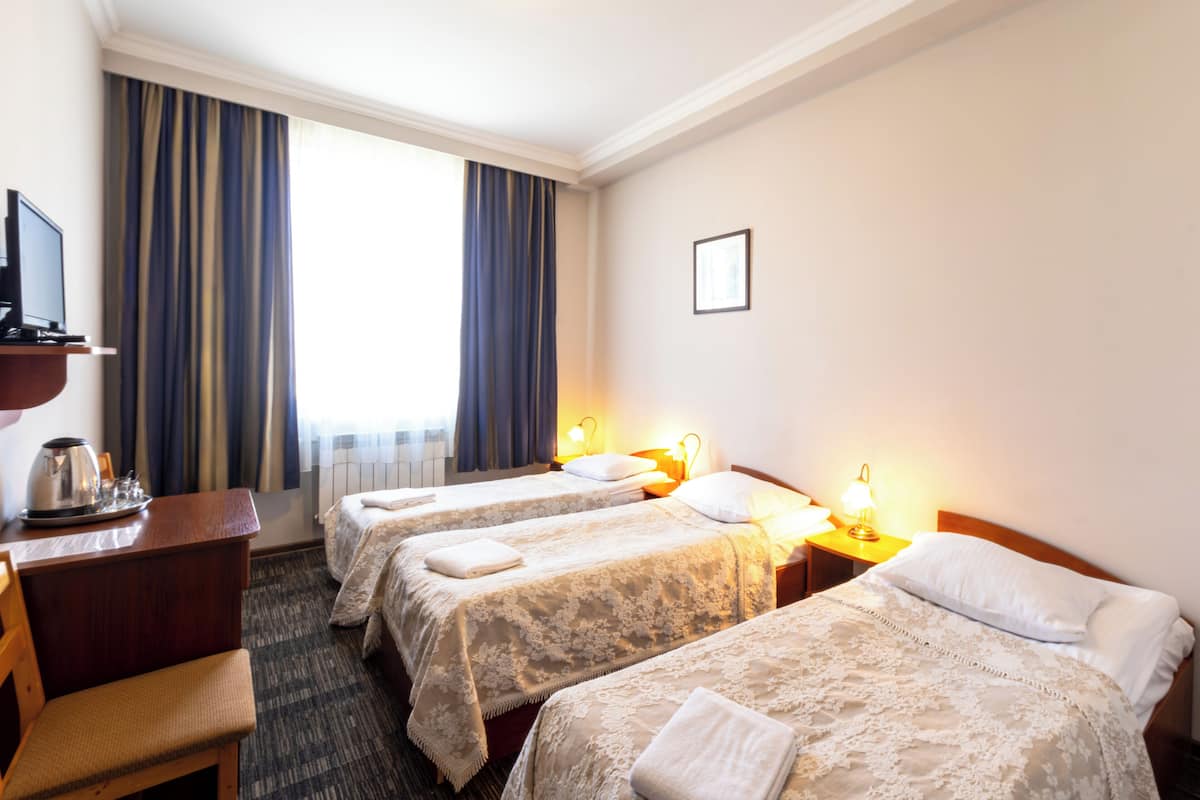 Habitación de hotel con tres camas, un escritorio con hervidor y televisión.