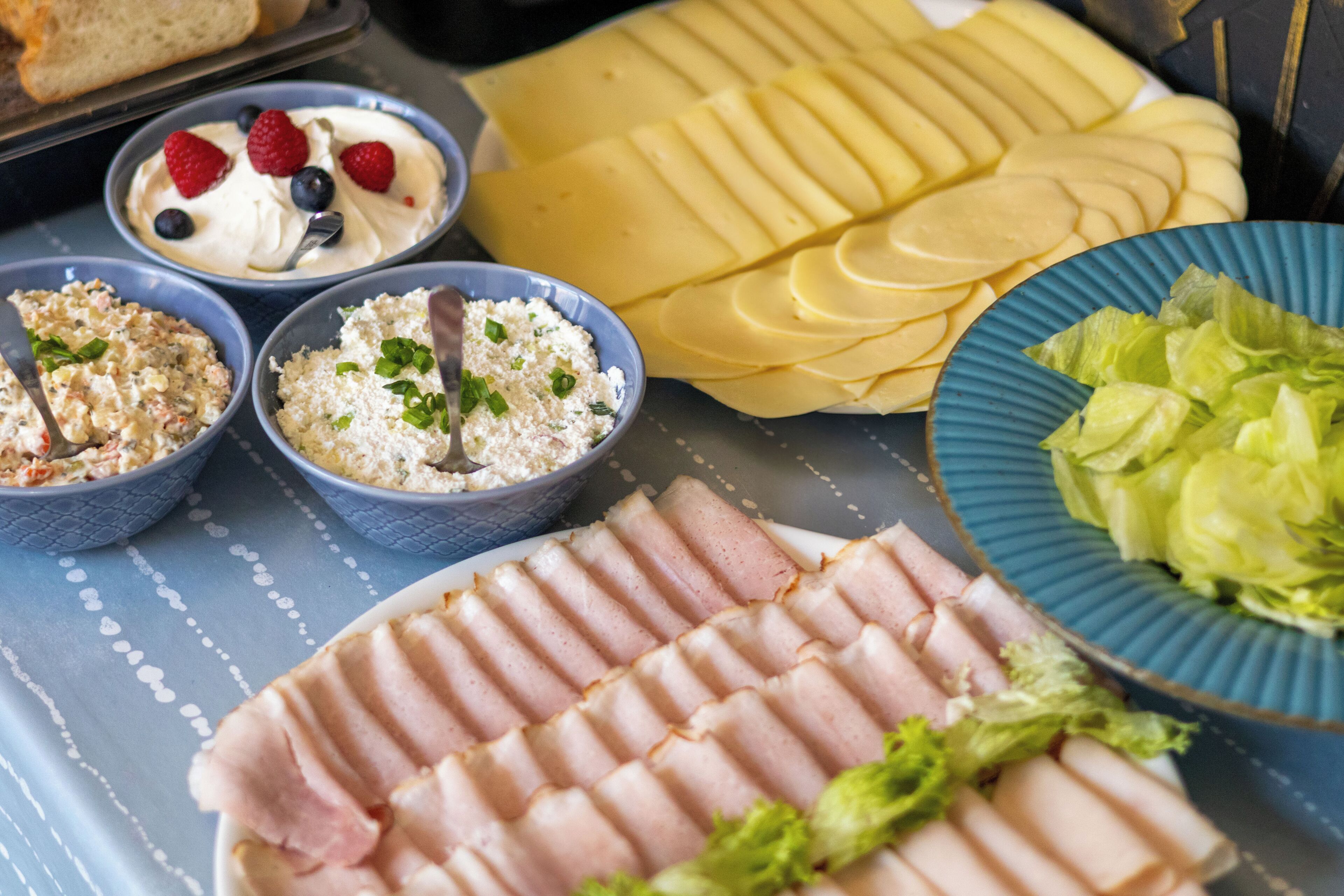 Ein Tisch mit verschiedenen Speisen, darunter geschnittenem Schinken, Käse sowie Schüsseln mit Salat und Dips.