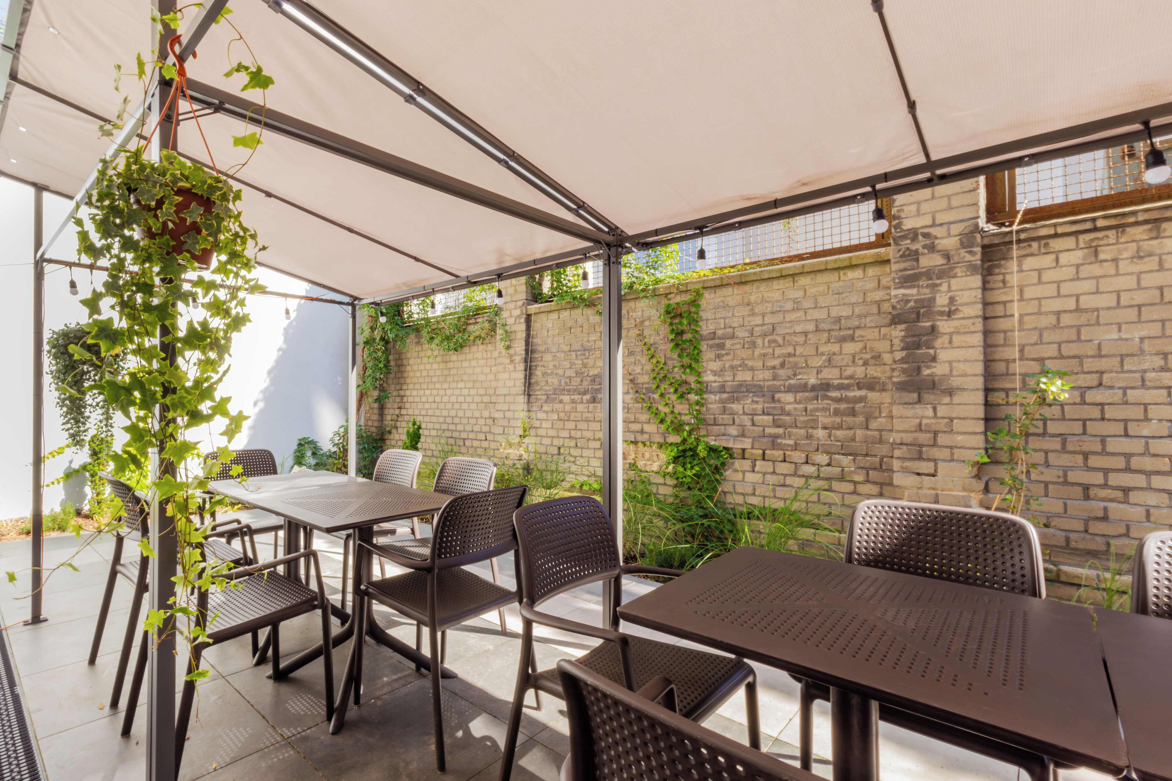 Une terrasse extérieure avec des tables et des chaises en métal, un mur de briques et de la verdure qui y pousse.