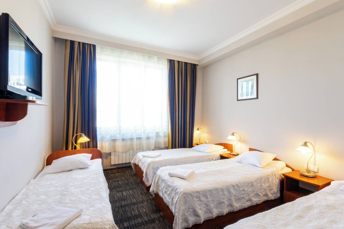 Habitación de hotel con dos camas, televisión y ventana con cortinas.