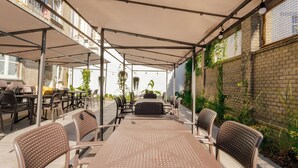 Une terrasse extérieure avec des tables et des chaises, un espace abrité et un mur de briques agrémenté de verdure.