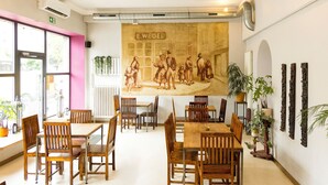 Un espace repas avec des tables et des chaises en bois, une fresque murale et des plantes en pot.