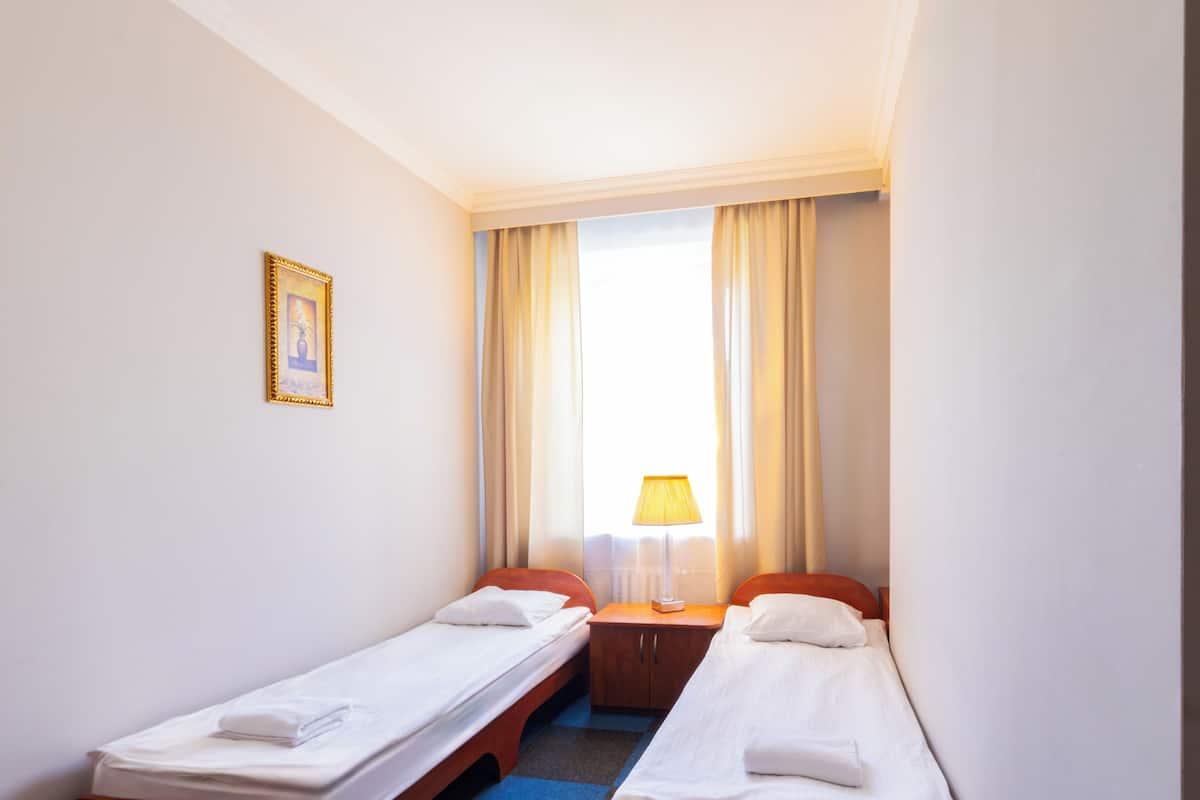 Una habitación de hotel con dos camas individuales, una mesita con lámpara, un cuadro enmarcado en la pared y una ventana con cortinas.