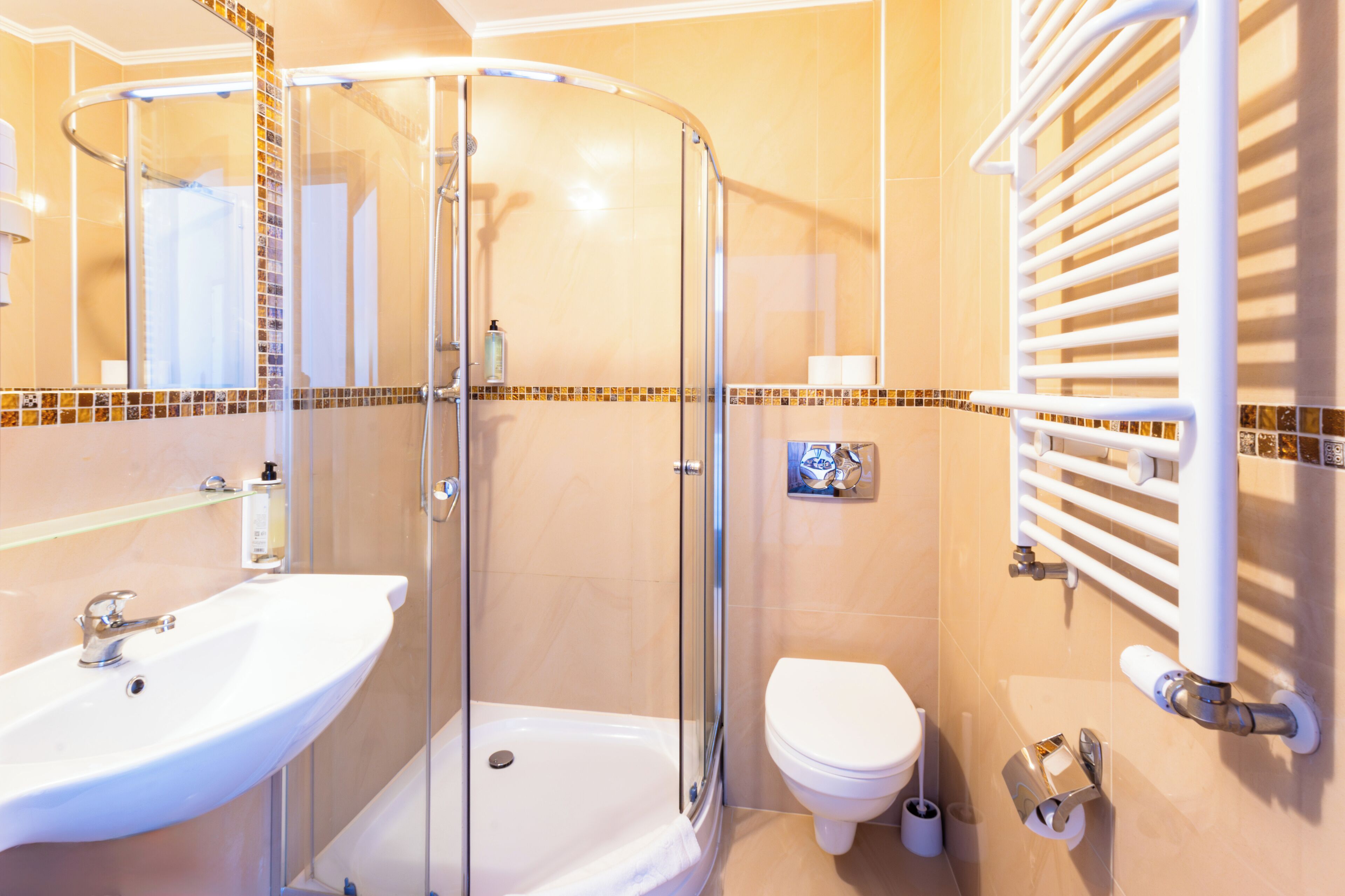 Baño con ducha envuelta en vidrio, lavamanos, inodoro y perchero para toallas.