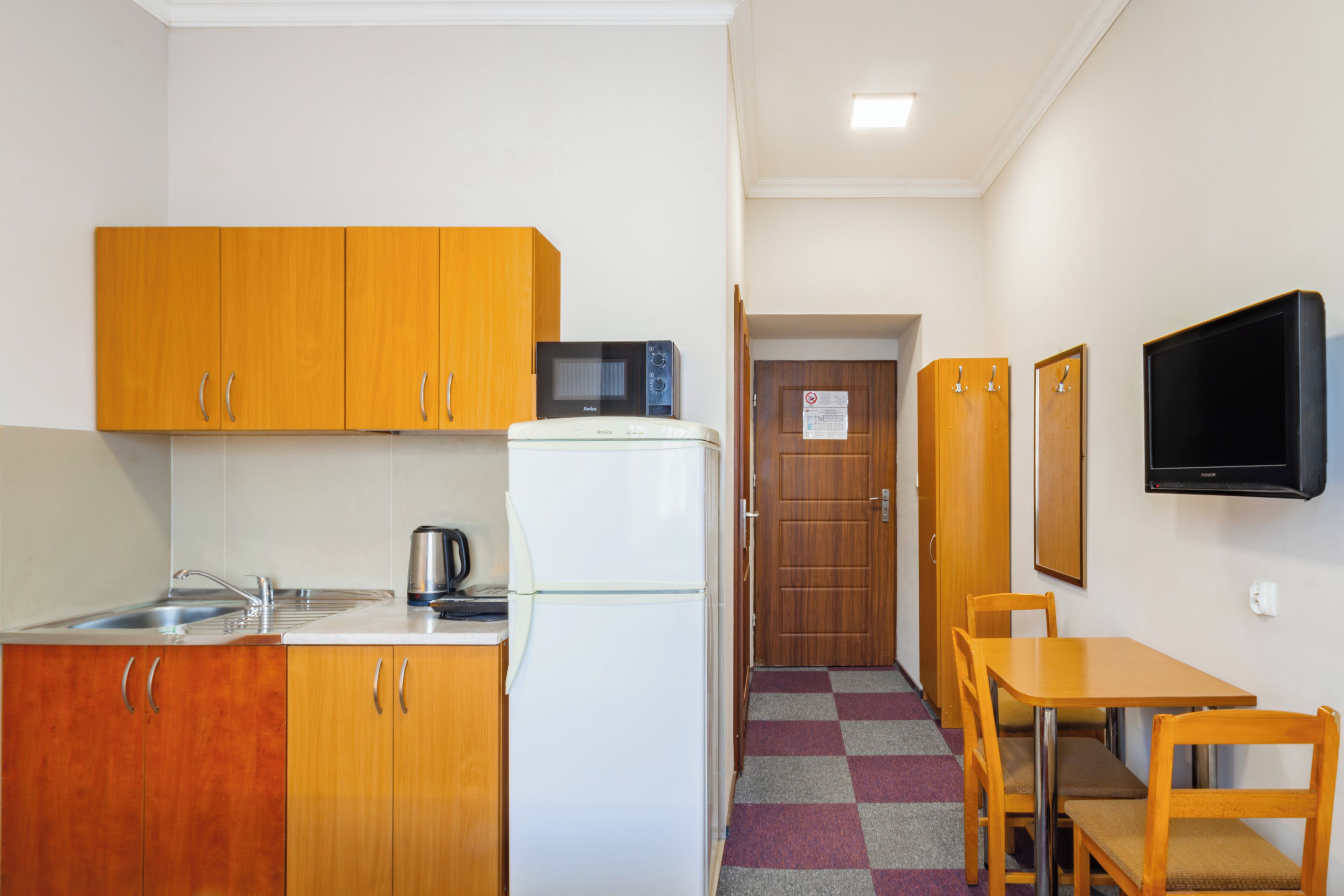 Una cocina compacta con armarios de madera, un refrigerador blanco, un microondas y un fregadero.