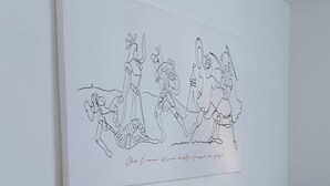 Et soveværelse med en seng, hvidt sengetøj, en sengegavl, et natbord og et billede på væggen, der viser en gruppe mennesker.