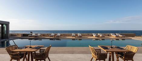 Un espace aménagé au bord de la piscine, avec une table et des chaises, une piscine et des chaises longues donnant sur l’océan.