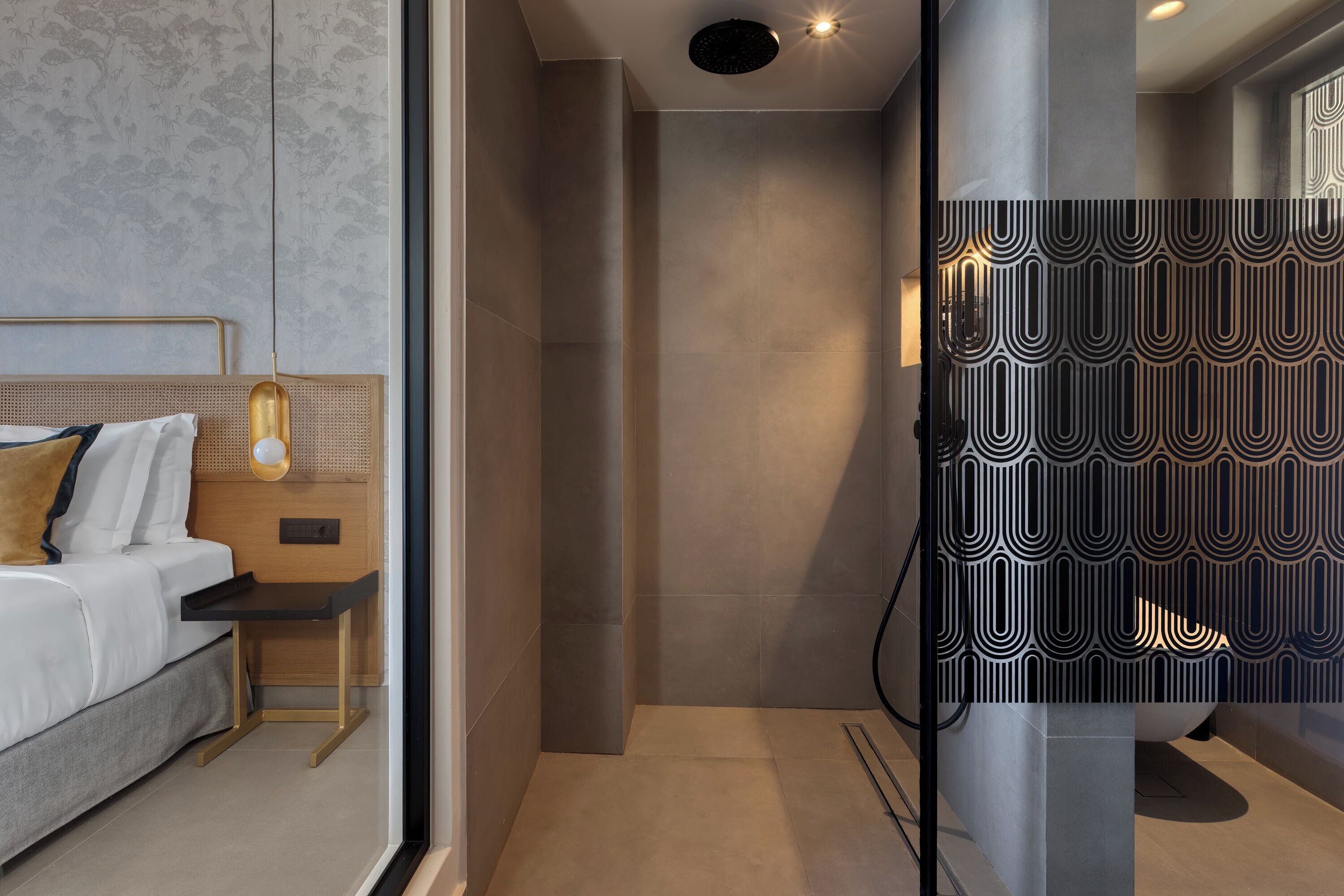 A modern hotel room with a bed, bedside table, and a shower area with a patterned wall.