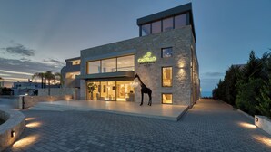 Un edificio moderno con fachada de piedra, ventanas grandes y un letrero de neón que dice "CASTELLO BOUTIQUE SUITES by the sea".