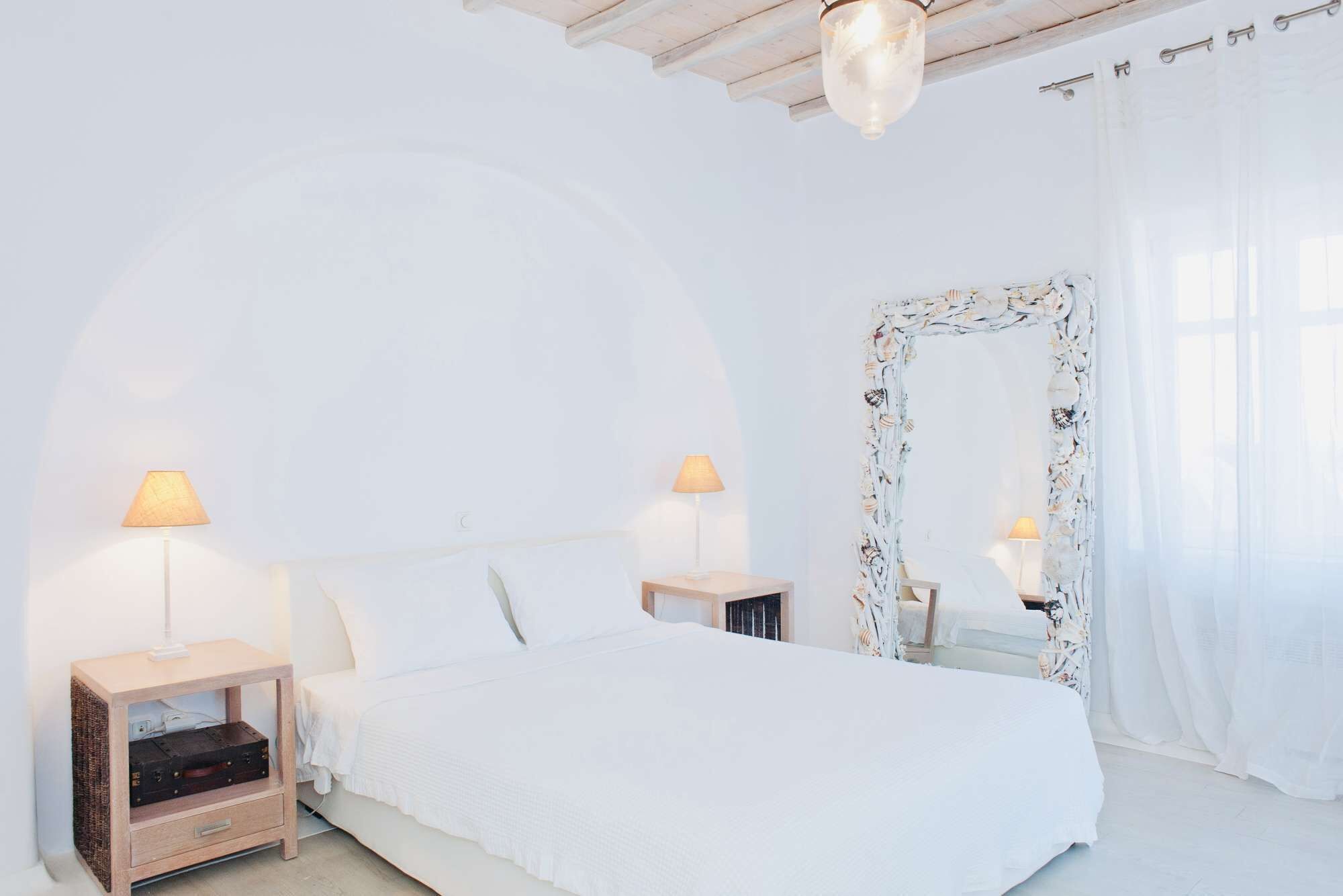 Un dormitorio minimalista con una cama grande, dos mesitas de noche con lámparas, un espejo decorativo y un arco blanco sobre la cama.