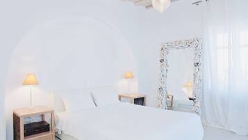 Un dormitorio minimalista con una cama grande, dos mesitas de noche con lámparas, un espejo decorativo y un arco blanco sobre la cama.