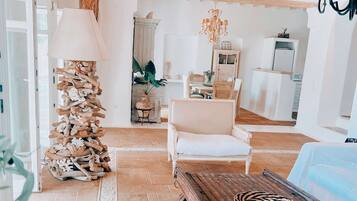 Un salón amplio con techo de madera, un sofá blanco, una mesa de centro y un comedor con mobiliario de mimbre.