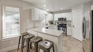 A modern kitchen with white cabinets, a central island with stools, a microwave, stove, and refrigerator. - 2 Story Home in Round Rock Sleeps 16 Guests (Round Rock)