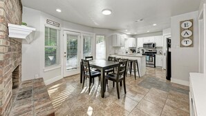 A modern kitchen with white cabinets, a dining table with chairs, and a brick fireplace. - 2 Story Home in Round Rock Sleeps 16 Guests (Round Rock)