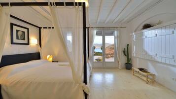 Een bed met hemel, een lijst met afbeelding aan de muur, een bedlamp, een cactusplant en een houten bankje met een schaal fruit.