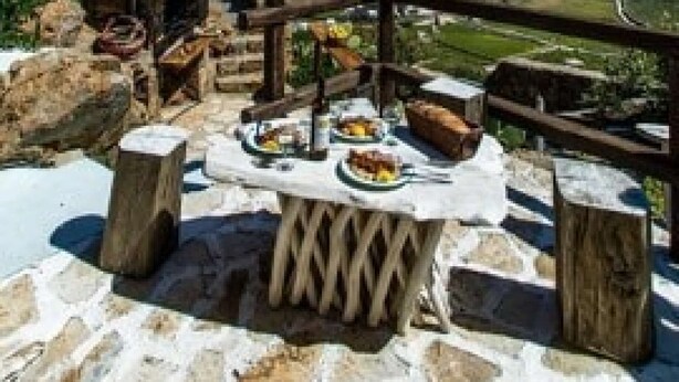 Ein Steintisch mit rustikalem Ambiente, mit Blick auf eine Küstenlandschaft und freiem Ausblick auf Meer und Hügel.