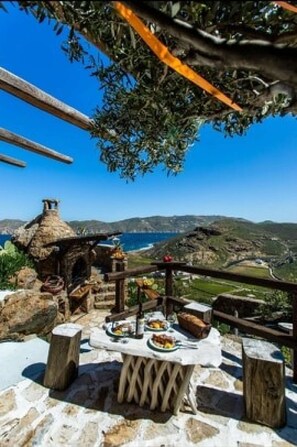 A stone table with a rustic setting, overlooking a coastal landscape with a clear view of the sea and hills. - Villa Princess 5 4Bed with Small Tub Panormos Beach (Mykonos)